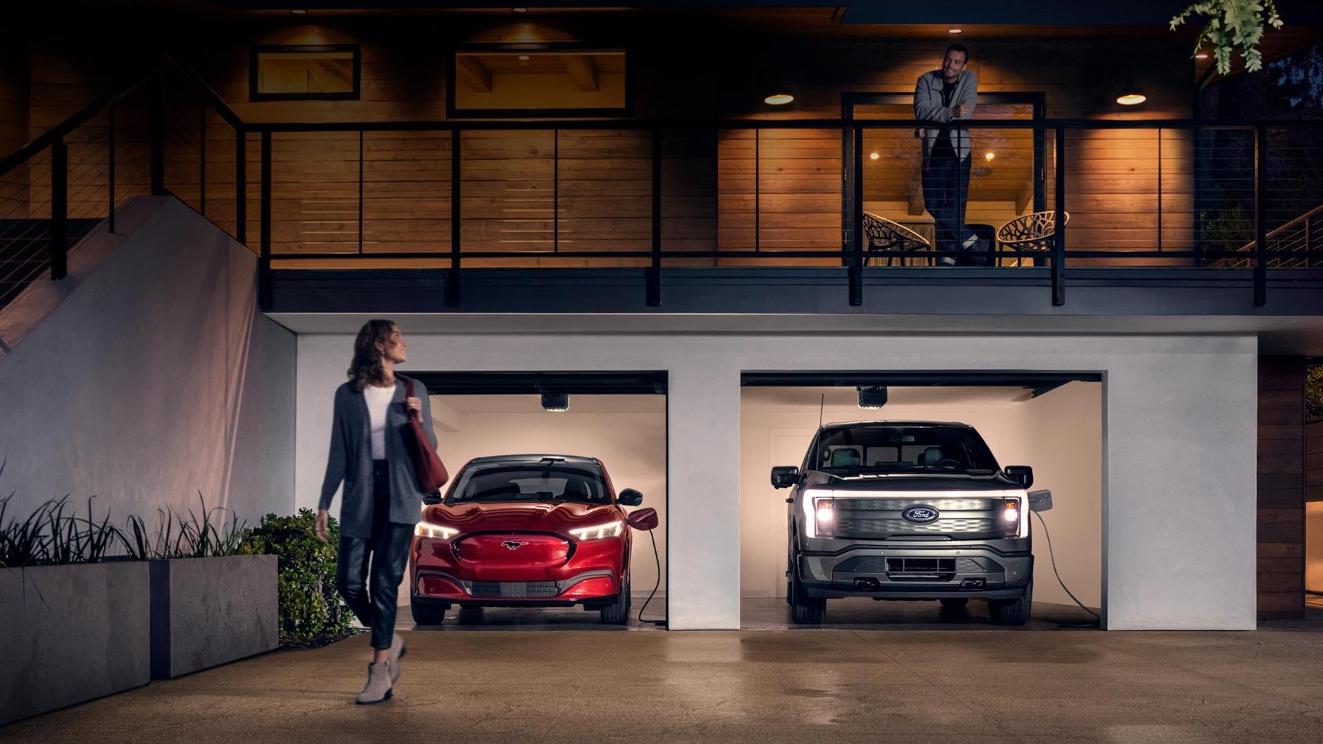 Woman walking out from home garage with a 2024 Mustang® Mach-E and Ford Lightning® truck in plugged-in and charging | C. Harper Ford in Belle Vernon PA